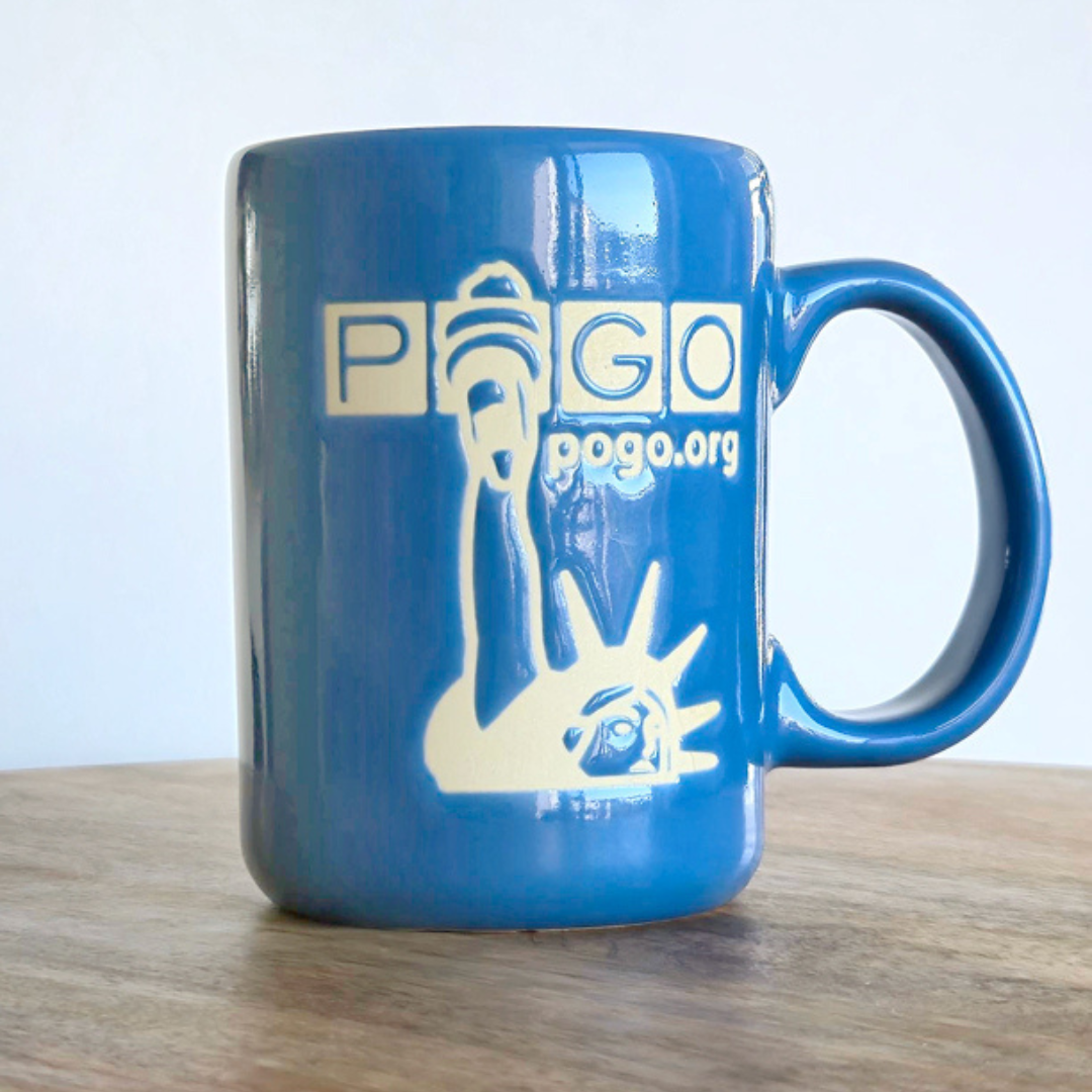 Blue glazed ceramic mug on a wooden table. The mug has a tall handle and a matte off-white design of unglazed clay showing the Statue of Liberty, POGO logo, and text: pogo.org.